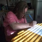 A woman writing on a piece of paper in front of a window.