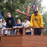 A group of people standing on the deck of a wooden pirate ship.