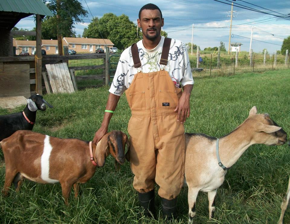 A man in overalls standing next to two goats.