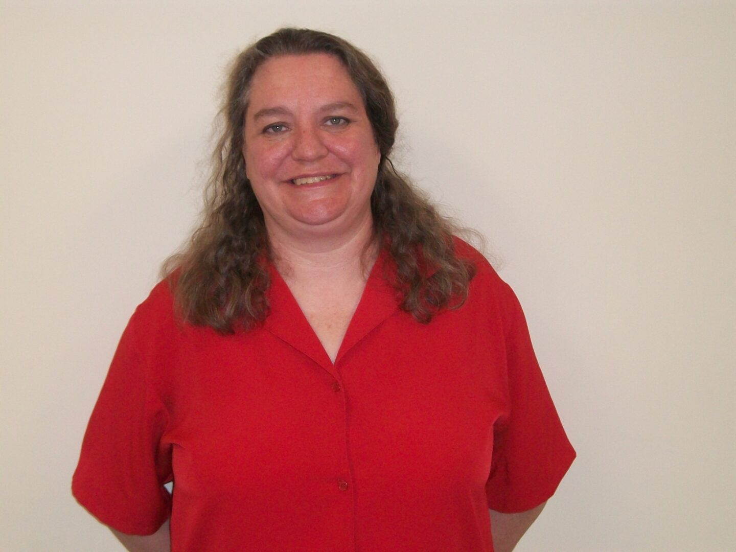 A woman in a red shirt smiling in front of a white wall.