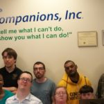 A group of people posing for a picture in front of a sign that says my companions inc.