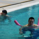 Two people swimming in an indoor pool with pink floats.