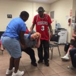 A group of people in a room with a man in a red shirt.