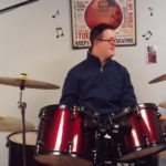 A man in glasses playing drums in a recording studio.