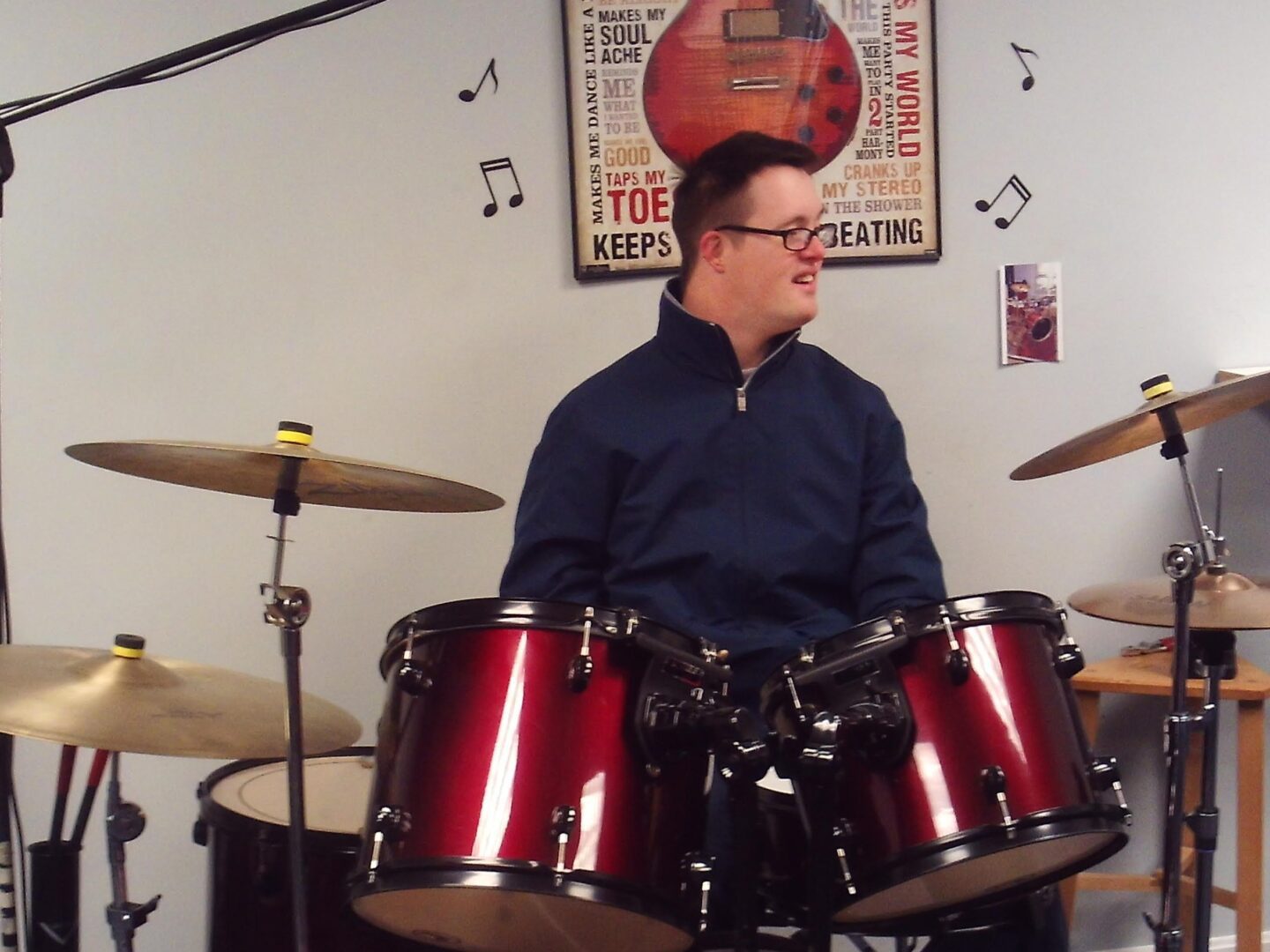 A man in glasses playing drums in a recording studio.