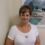 A woman in a white shirt standing in front of a sign for daily companions.