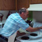 The man is wearing a plaid shirt while engaging in residential living.