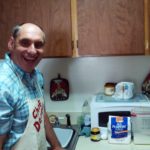 A man in a plaid apron resides in a residential living setting.