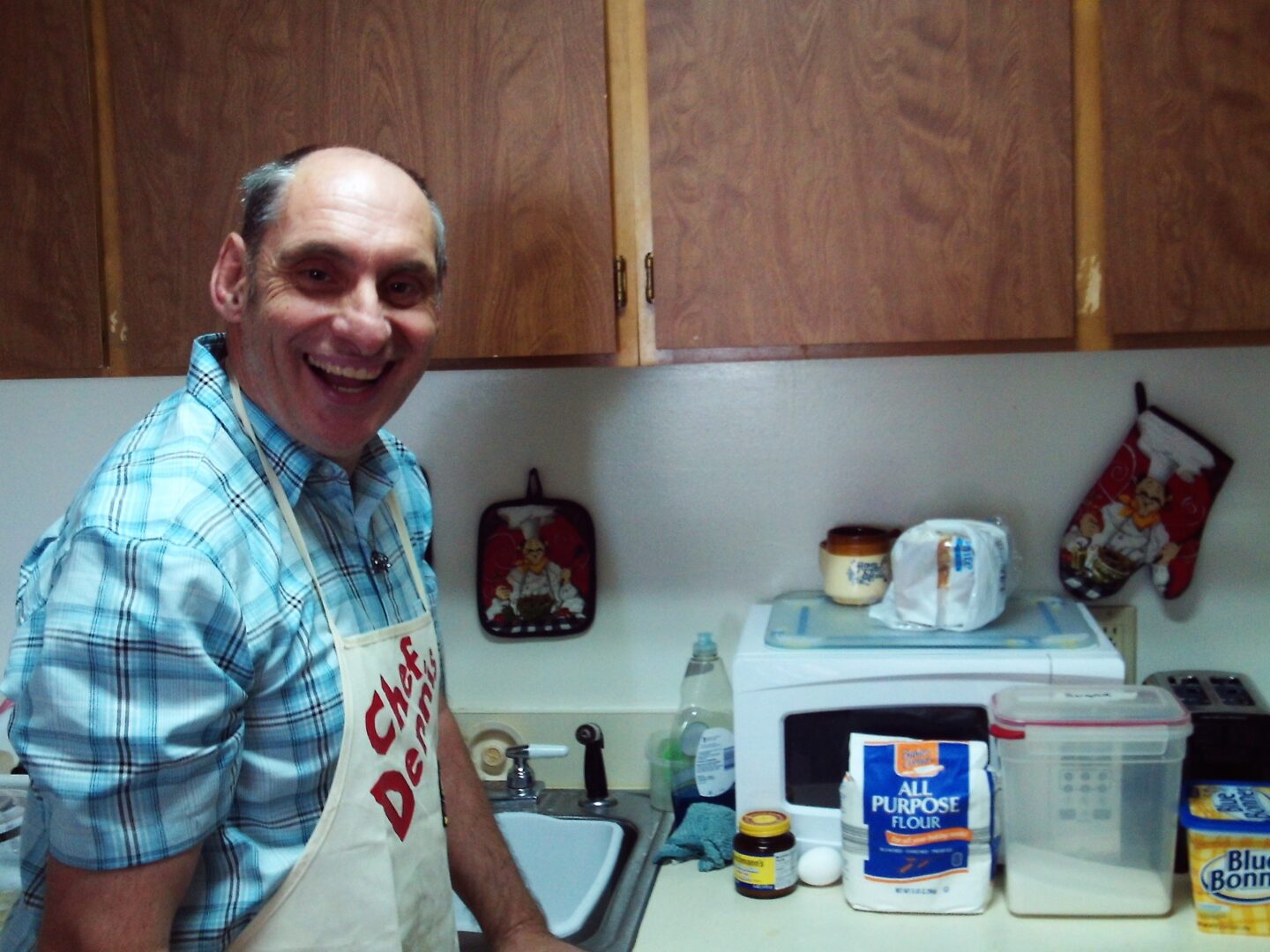 A man in a plaid apron resides in a residential living setting.