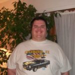 A man in a t - shirt standing in front of a car.