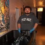 A man holding a trash can in a hallway.