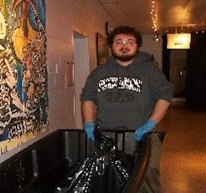 A man holding a trash can in a hallway.