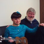 A man and a girl sitting on a couch with a ukulele.